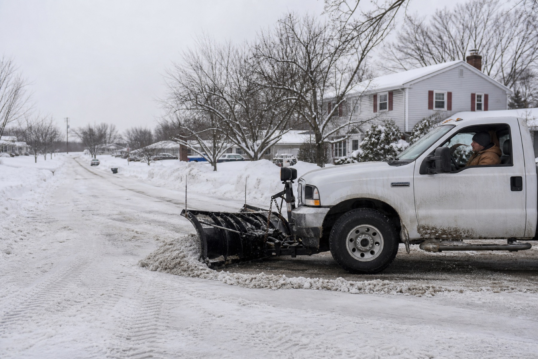 White pickup with a plow pushing slush down a suburban street on an overcast winter morning